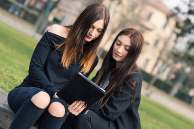 Parkta tablet kullanan genç kız kardeşlerin portresi..