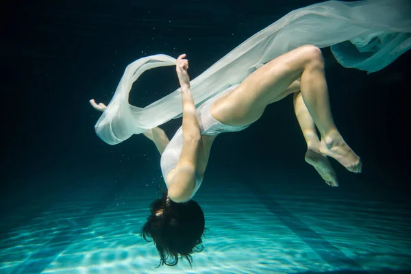 Underwater woman upside down portrait in swimming pool at night.