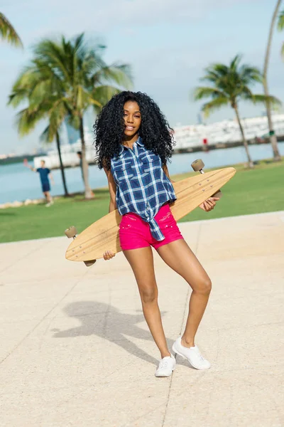 Happy young woman full body portrait holding long board in South