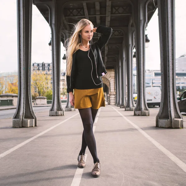 Young beautiful woman full body portrait listening to music with headphones while walking under Bir Hakeim bridge in Paris, France.