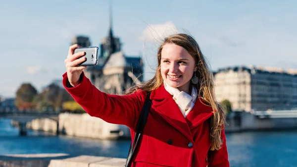 Szczęśliwy młody Blondynka kobieta biorąc a selfie z Notre Dame CATHEDR — Zdjęcie stockowe