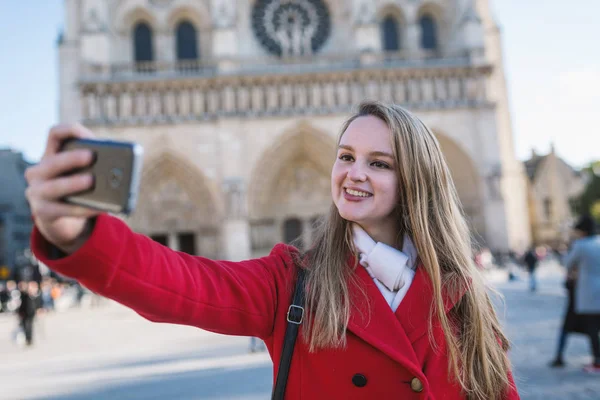 Young blonde woman taking a selfie with Notre Dame Cathedral in — 스톡 사진