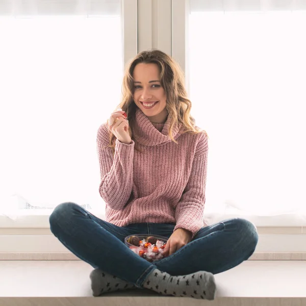 チョコレートキャンディを食べながら 自宅で笑顔の若い女性の肖像画 — ストック写真