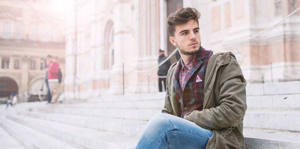 Young man portrait sit on the stairs in front of San Petronio Cathedral in the city center of Bologna, Italy. Concept of urban lifestyle.