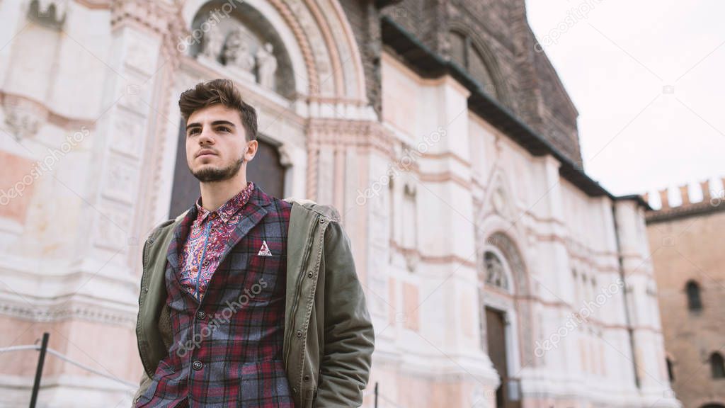 Young confident man standing in front of San Petronio Cathedral, Bologna, Italy.