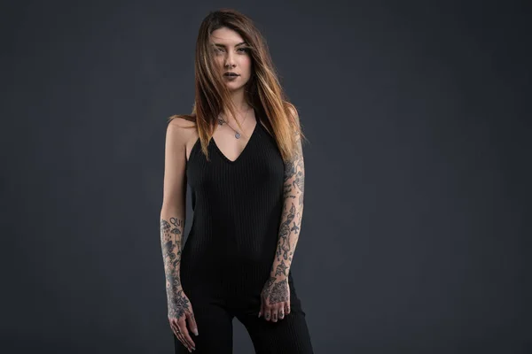 Confident woman studio portrait with long black dress and tattoo