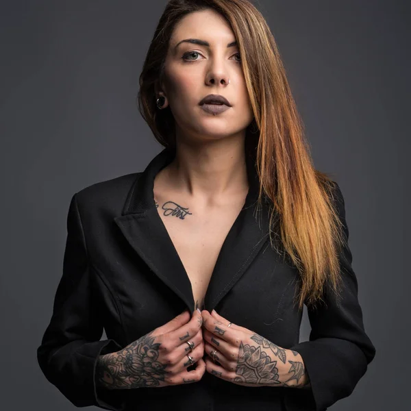 Confident woman portrait with long black dress and tattoos.