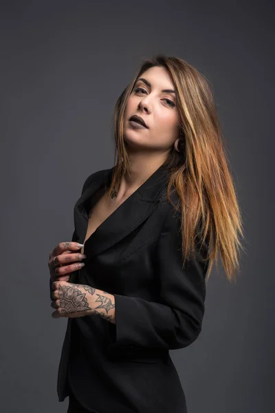 Confident woman portrait with long black jacket and tattoos.
