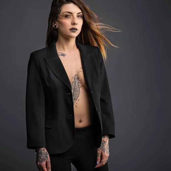 Confident woman portrait with long black dress and tattoos.