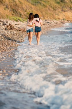 Genç kız kardeşler denizde sarılıp yürüyorlar, arkadan görüyorlar. Yaşam tarzı kavramı.