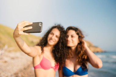 Genç kız kardeşler denizde fotoğraf çektirirken birlikte eğleniyorlar. Yaşam tarzı konsepti. Telefona odaklan..