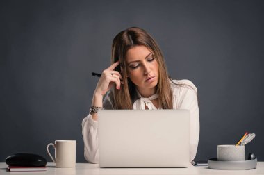 Young businesswoman sit at desk thinking to a solution studio portrait against grey background.