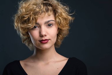 Confident young woman studio head portrait against black background.