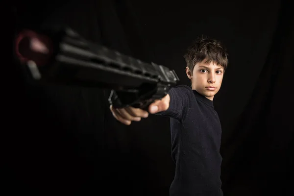 おもちゃの銃を指す激しい子供 黒い背景に対するスタジオの肖像画 — ストック写真