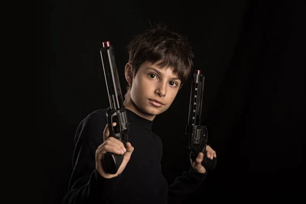 Fierce kid holding toy guns. Studio portrait against black background.