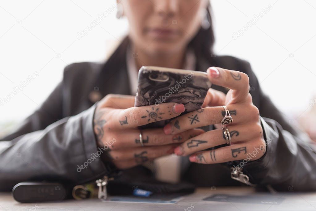 Young tattooed woman hands close up using smartphone.