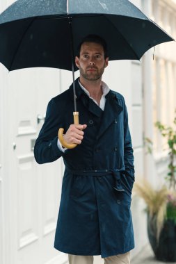 Confident elegant businessman holding umbrella while raining in London city. United Kingdom.