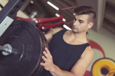 Young sporty man portrait working out in the gym preparing wheights for squats. Concept of active lifestyle.