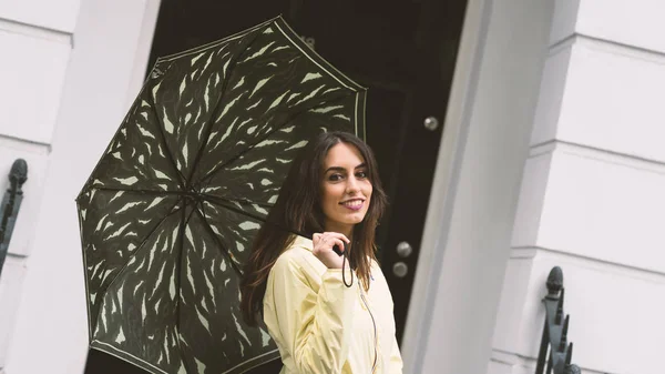 Smiling woman under the rain with umbrella in Notting Hill district. London, UK. Lifestyle portrait.