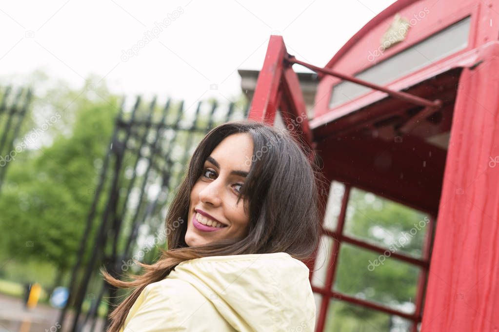 Happy young woman portrait close to red telephone box in London.