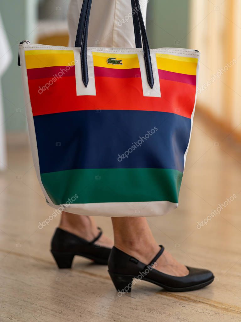 Cropped shot of female feet and Colorful Lacoste purse with logo