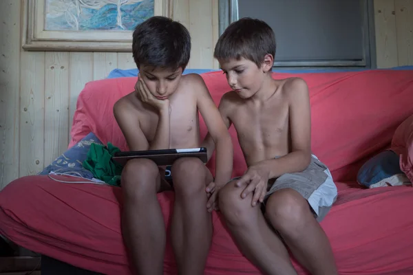 Молоді брати діти використовують планшет вдома, сидячи на дивані . — стокове фото