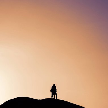 Turuncu gökyüzüne karşı bir kayanın üzerinde tanımlanamayan bir çiftin silueti. Filtrelenmiş resim instagram biçimi.