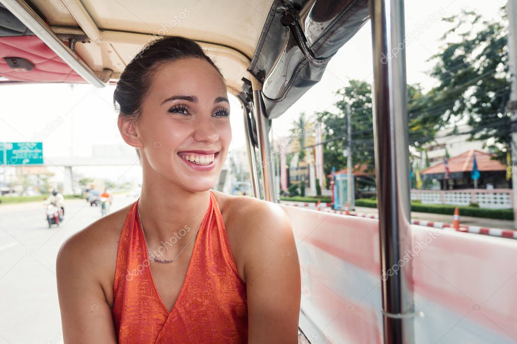 Smiling young woman portrait inside Tuk Tuk in the street. Auto rickshaws are the fastest ways of getting around congested Bangkok streets. 