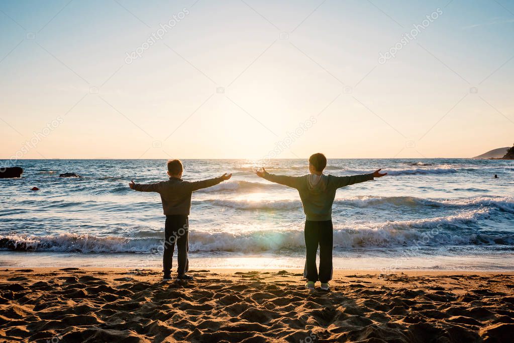 Young brothers silouette portrait in front of the sea at sunset.