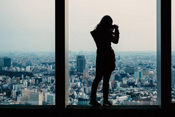 Woman silhouette taking a photo with camera at Observation Deck. Tokyo, Japan.