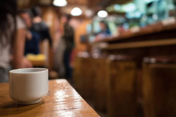 背景に焦点が合っていないレストランを持つ日本酒カップ — ストック写真