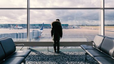 Çocuk bekleme odasında durmuş ve uluslararası havaalanındaki uçaklara bakıyor. Seyahat ve tatil için kavramsal resim.