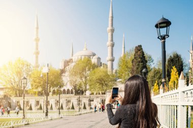 Mavi Cami 'nin akıllı telefonuyla fotoğraf çeken genç bir kadın. İstanbul, Türkiye.