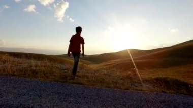 Çocuk silueti kollarını açıyor ve gün batımında sonsuzluğa bakıyor. Kavramsal görüntüler.