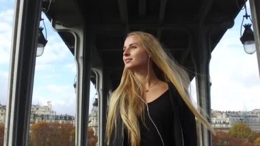 Paris, Fransa 'da Bir Hakeim köprüsünün altında yürürken kulaklıkla müzik dinleyen güzel sarışın kadın portresi..