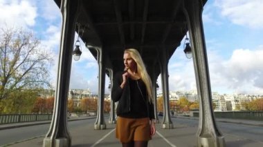 Paris, Fransa 'da Bir Hakeim köprüsünün altında yürürken kulaklıkla müzik dinleyen güzel sarışın kadın portresi..