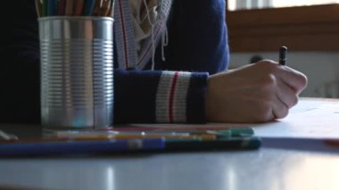 Close-up of woman drawing with pencil at home.