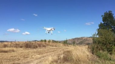 Beyaz kuadkopter kuru kırlarda uçuyor. 