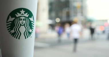 logolu starbucks kahve kağıt fincan ve arka planda insanlar hareketli
