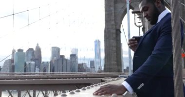 Takım elbiseli genç işadamı Brooklyn Köprüsü, New York 'ta akıllı telefondan konuşuyor. 