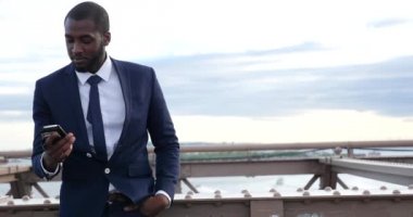 Takım elbiseli genç işadamı Brooklyn Köprüsü, New York 'ta akıllı telefondan konuşuyor. 