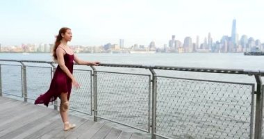 New Jersey rıhtımı boyunca dans eden genç, güzel balerin New York silueti arka planda.
