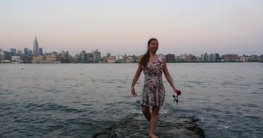 New Jersey rıhtımı boyunca dans eden genç, güzel balerin New York silueti arka planda.