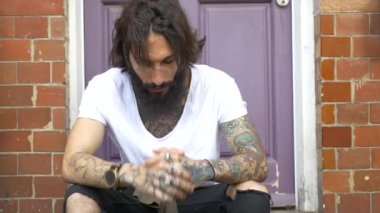 Shoreditch ilçesinde sokakta oturan dövmeli genç bir adamın yoğun görüntüleri. Londra, İngiltere. Hipster tarzı