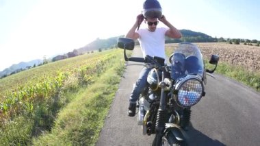 güneşli bir günde çayır arasında motosiklet üzerinde otururken güvenlik kaskı giyen beyaz t-shirt giyen yakışıklı sportif adam   