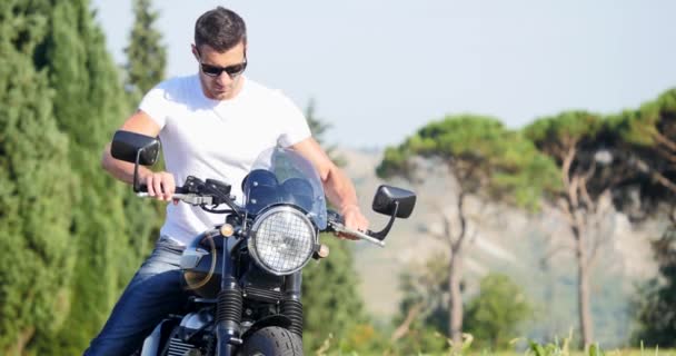 英俊的运动男子穿着白色T恤开始和骑摩托车在草地在阳光明媚的一天 — 图库视频影像