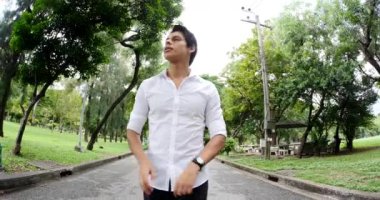 Yeşil parkta yürüyen beyaz gömlekli genç adam.