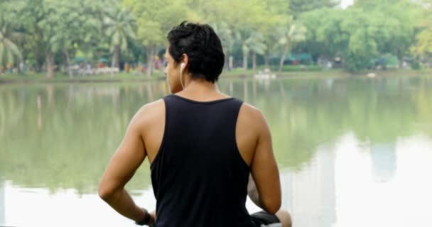 Joven Sentado Junto Lago Con Smartphone Auriculares — Vídeo de stock