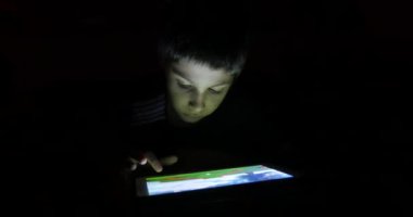 Küçük çocuk geceleri yatakta tabletle oynuyor..