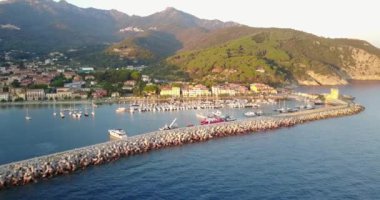 güneşli deniz manzara, limanda demirlemiş tekneler, şehir binaları ve yeşil tepeler